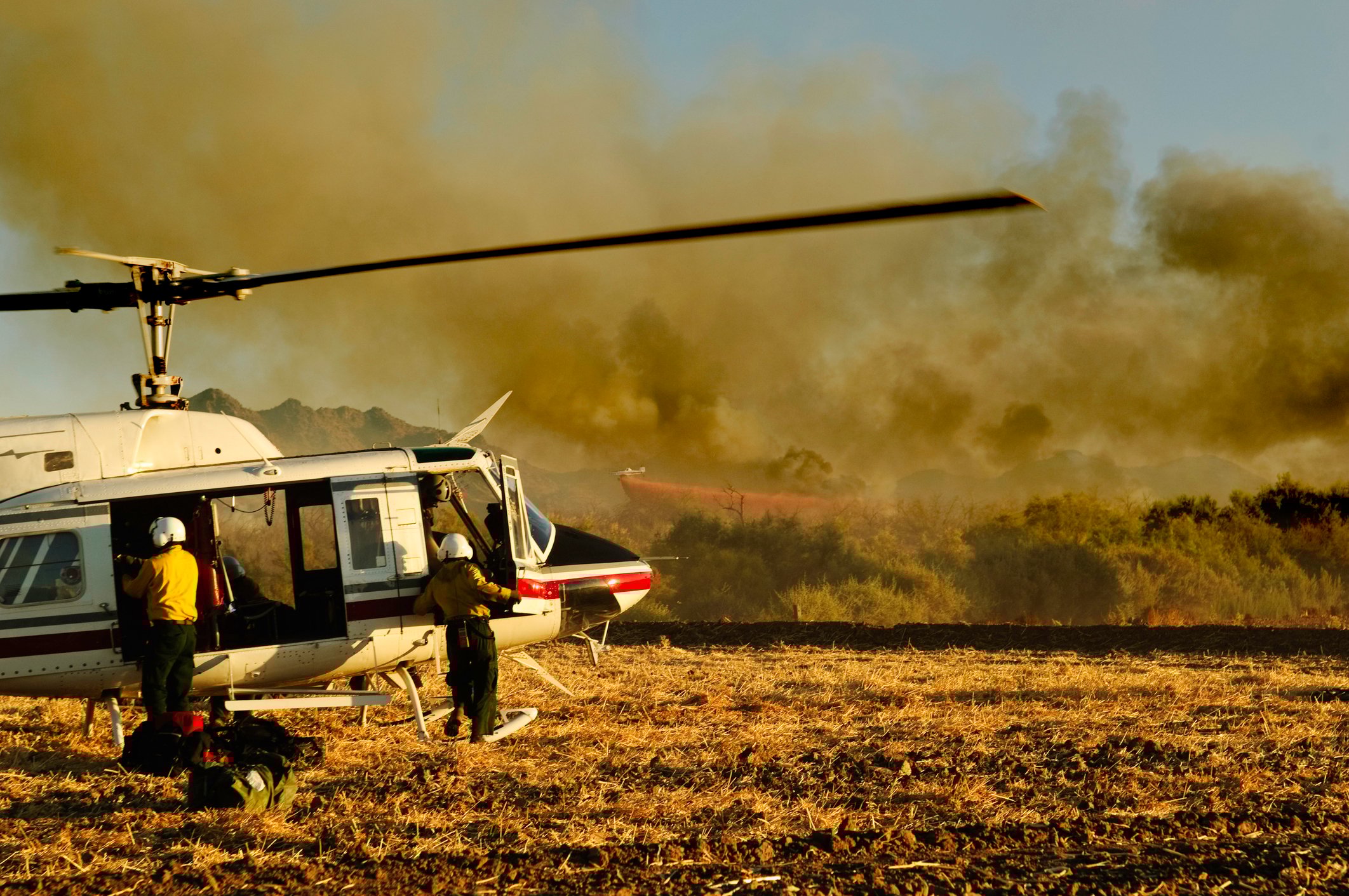 helicopter in an active wildfire zone with an aircraft flying behind, dropping extinguishing liquids.